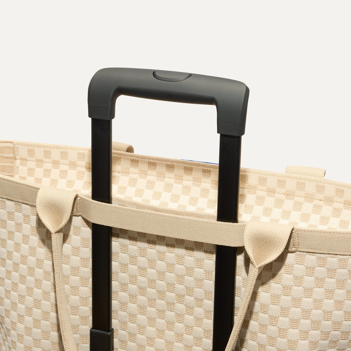 The Zip Travel Tote in Parchment Basketweave, shown attached to a rolling suitcase using the wrap-around band.