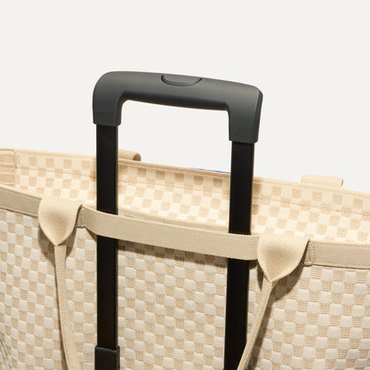 The Zip Travel Tote in Parchment Basketweave, shown attached to a rolling suitcase using the wrap-around band.
