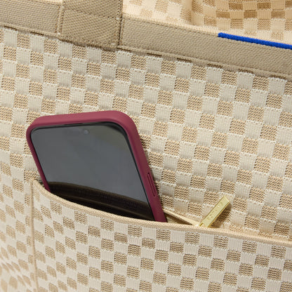 A close up of The Zip Travel Tote in Parchment Basketweave with a phone slipped into the outer pocket.A close up of The Zip Travel Tote in Parchment Basketweave with a phone slipped into the outer pocket.